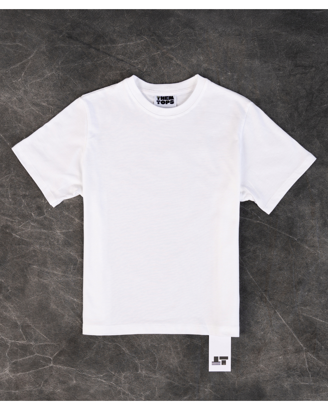 A plain white short-sleeve crewneck t-shirt laid flat on a dark textured gray background. 