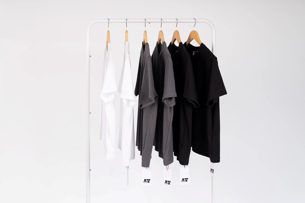 A white metal clothing rack holding five short-sleeve shirts in white, gray, and black, suspended from wooden hangers against a plain white background.