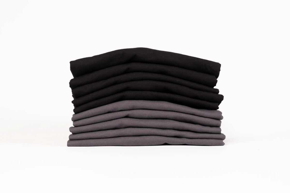 A stack of neatly folded t-shirts in a gradient of black, dark gray, and medium gray, set against a plain white background.